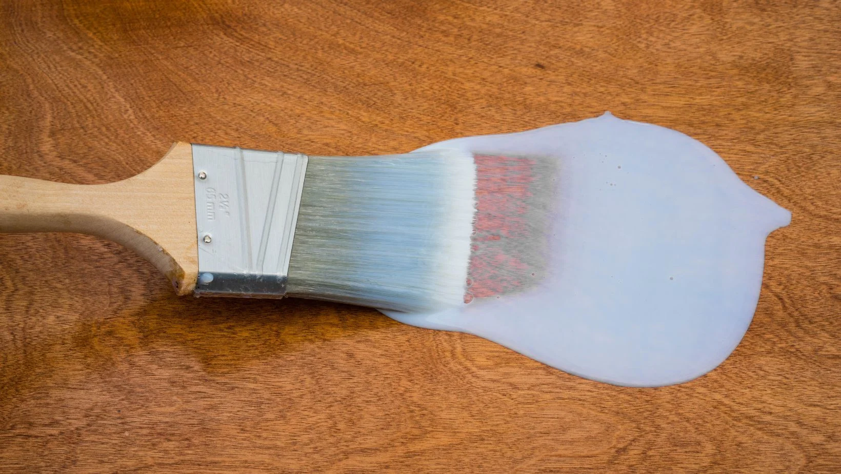 A paint brush with polyurethane on hardwood flooring