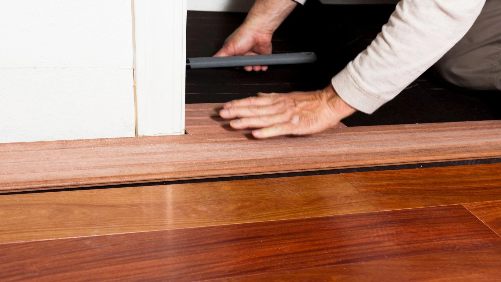 A person installing hardwood flooring against a wall